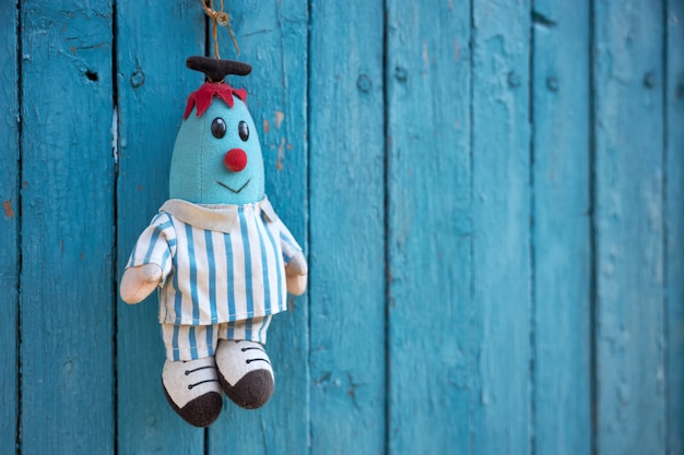 Faded soft doll in the shape of a blue man hangs on a blue wooden fence