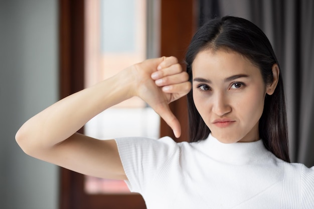 写真 失敗した女の子が親指を下に向ける不幸で動揺している女性の肖像画を下に向ける拒絶の親指を下に向けるアジアの中国人女性の若い大人のモデルによる悪い拒絶の親指を下に向けるジェスチャー