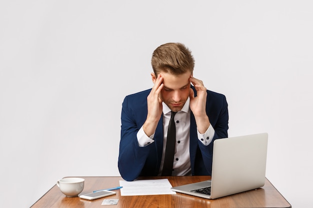 Failure, fatigue and depression concept. Man having bad day, feeling let down, losing important case in court, sitting office table with laptop and documents, touching temples, have headache