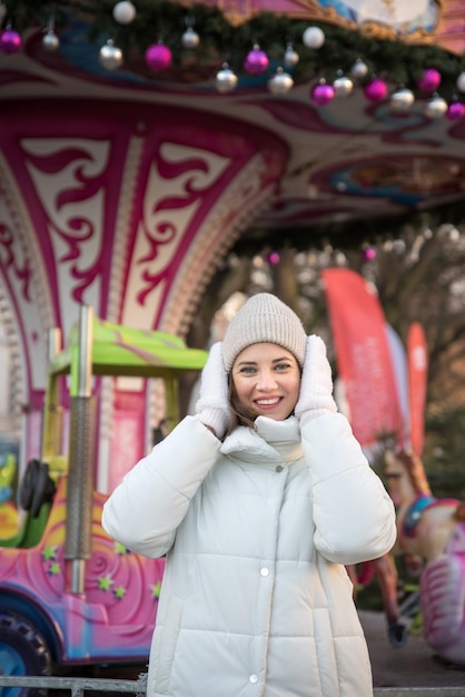 Fair attractions carousel girl dressed in a white jacket and a white hat the girl smiles girl rejoices emotions Celebrating Christmas outdoors