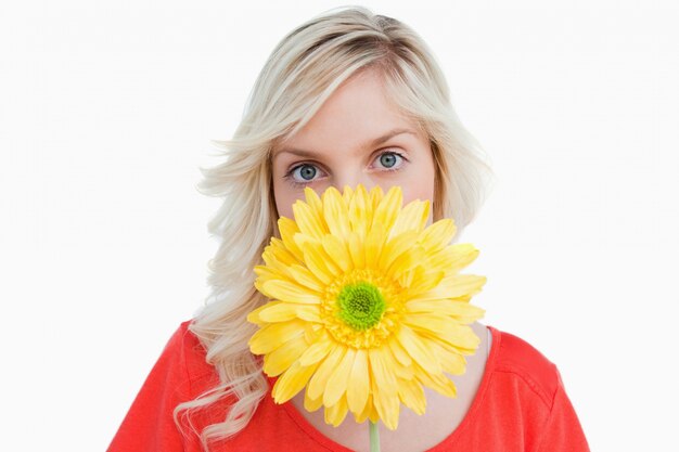 黄色の花の後ろに彼女の顔を隠すフェアヘアの女性