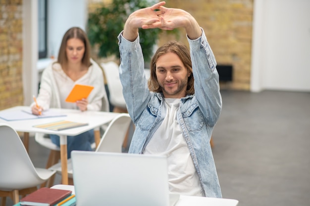 Foto biondo giovane uomo seduto al laptop e allungando le mani