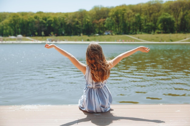 A fairhaired little girl sits on a pier by the water Cute little girl on the beach