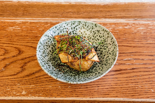 Photo fairstyle roasted potato with skin with wakame seaweed salad on green bowl with black pints on oak table