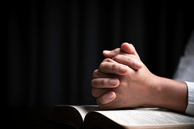 Faith with holy bible concept hands of a female prayer worship\
god with holy bible on black background in church christian woman\
who believe in jesus read and study the grace of the holy\
scriptures