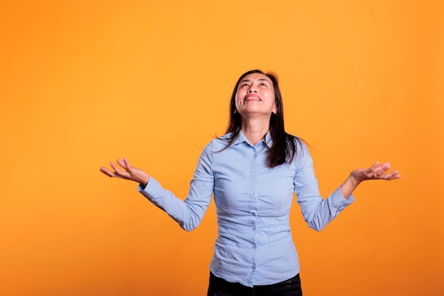 Faithful filipino woman standing with palms faced to sky, asking god for better life in studio over yellow background. hopeful religious young adult showing gratitude, praying for peace