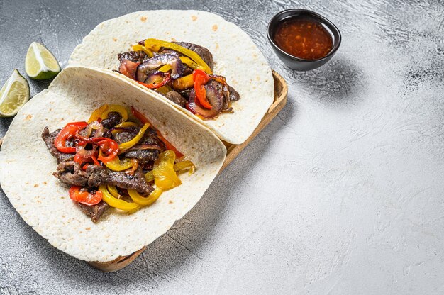 Fajitas met runderstrepen, gekleurde paprika en uien, geserveerd met tortilla's en salsa.