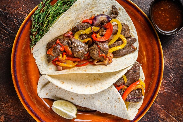Fajitas Tortilla wraps with beef meat steak stripes, sweet pepper and onions. Dark wooden table. Top view.