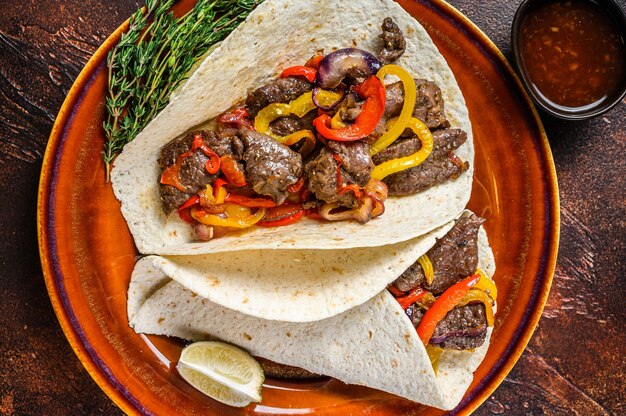 Fajitas Tortilla는 쇠고기 고기 스테이크 줄무늬, 달콤한 고추 및 양파로 포장됩니다. 어두운 나무 테이블. 평면도.