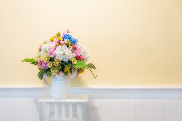 Fake flowers for interior decoration on white wood with cream wall in background.