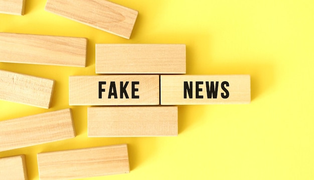 FAKE NEWS text written on a wooden blocks on a yellow background