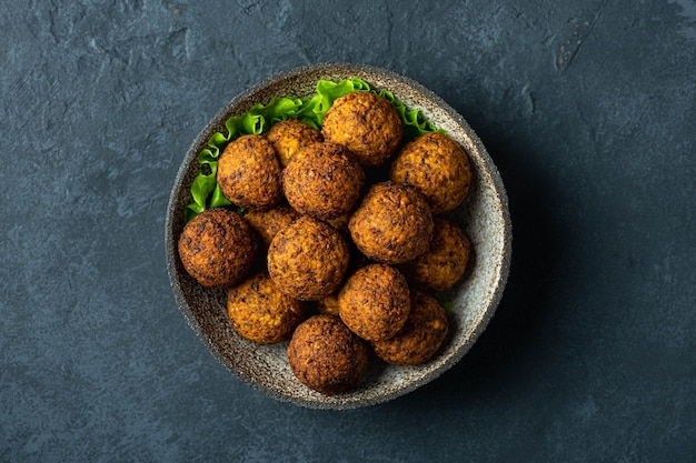 Falafel balls in a ceramic bowl on a black background top view