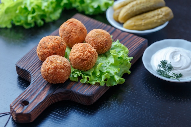 Falafel ligt op een houten snijplank. Op de tafel liggen tomaten, komkommers, sla, dille, citroen, zure room. Midden-Oosten nationale gerecht.