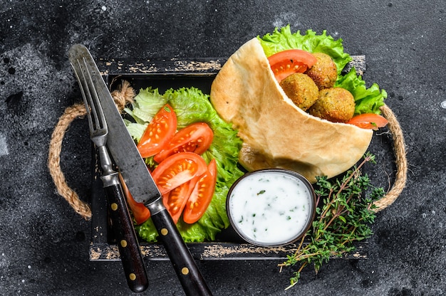 Falafel with vegetables, sauce in pita bread, vegetarian kebab sandwich. Black background. Top view.