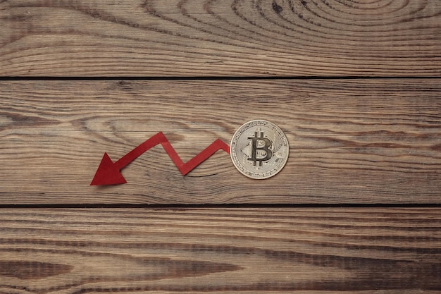 Fall arrow and golden bitcoin on a wooden table Falling bitcoin price