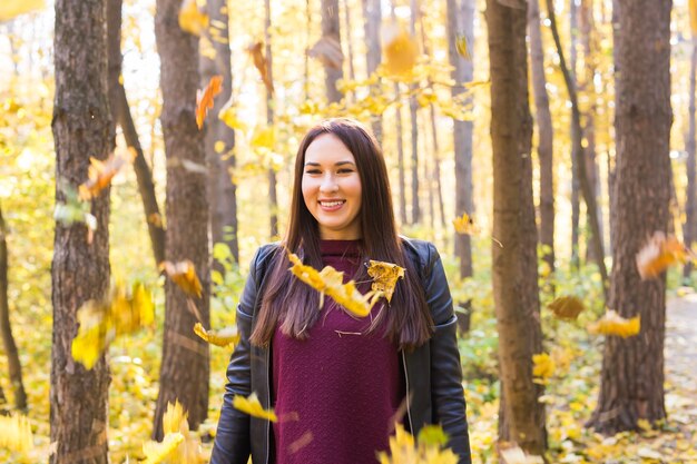 Fall, beauty, people concept - young woman posing in autumn park with falling leaves.