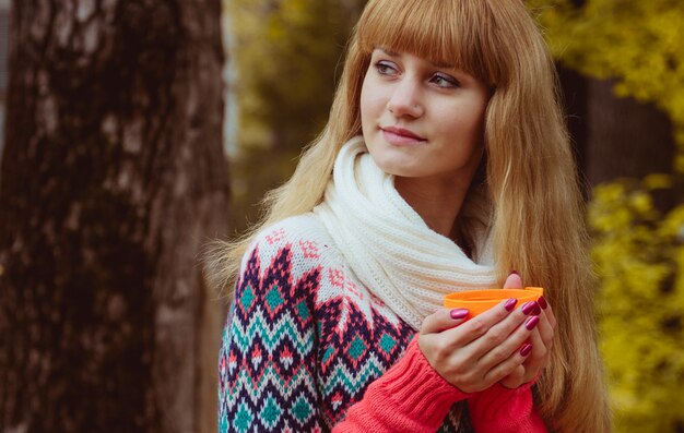 Fall concept - autumn woman drinking coffee in park