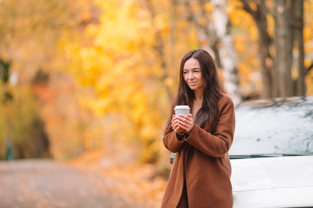秋のコンセプト-秋の紅葉の下で秋の公園でコーヒーを飲みながら美しい女性
