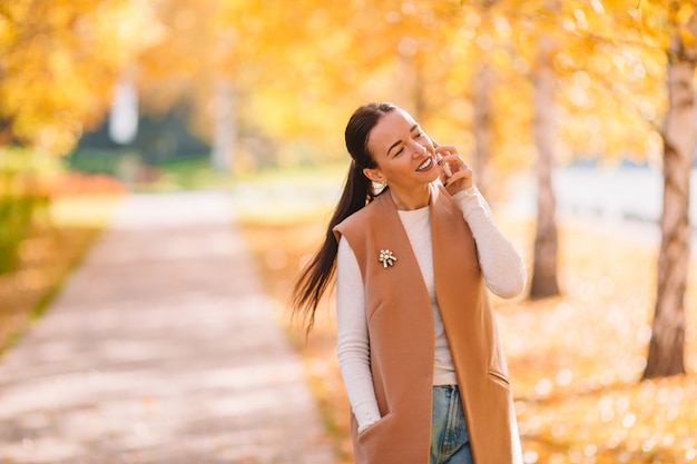 Fall concept - beautiful woman drinking coffee in autumn park under fall foliage