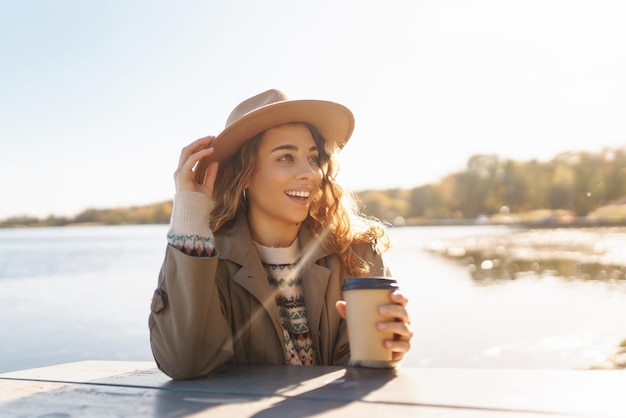 Fall concept vrouw drinkt koffie op een bankje tegen de achtergrond van het meer Geniet van eenzaamheid met de natuur