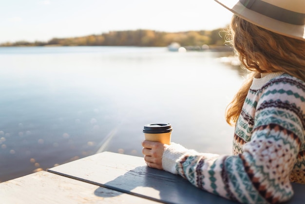 Fall concept vrouw drinkt koffie op een bankje tegen de achtergrond van het meer Geniet van eenzaamheid met de natuur