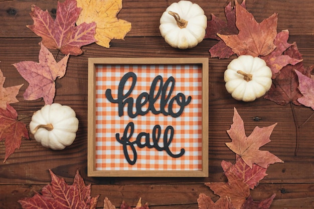 Photo fall flat lay with white pumpkins and colorful fall leaves and a sign that says hello fall