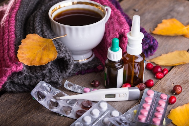 Fall and health care cup of tea pills and thermometer on a wooden backgroundxA