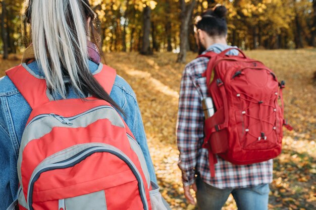 Fall journey Back view of couple traveling with backpacks in autumn nature park Trees and foliage background