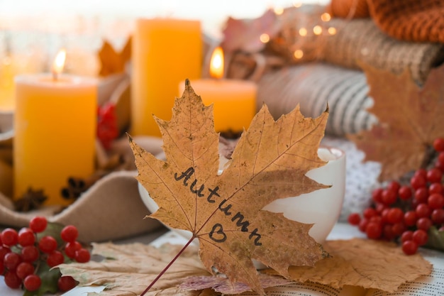 Fall maple leaf with text AUTUMN on Autumn season design concept Candles on windowsill rainy weather Warm Cozy hygge atmosphere