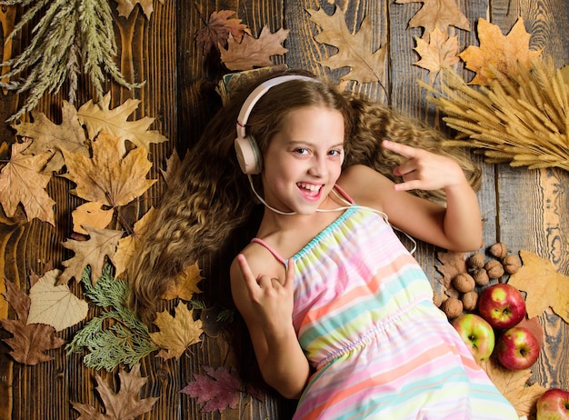 Playlist di musica autunnale canzone sull'autunno goditi la musica e rilassati ragazza posa foglie cadute sottofondo in legno applicazione musicale per giovani gadget moderni bambina ascolta musica cuffie vista dall'alto