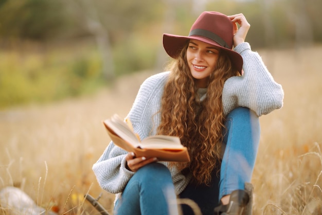 Fall picnic in nature Young woman sitting on the blanket reading a book and smiling outdoors