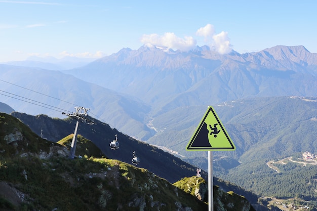 Segnale di avvertimento di caduta sullo sfondo delle montagne con la funivia