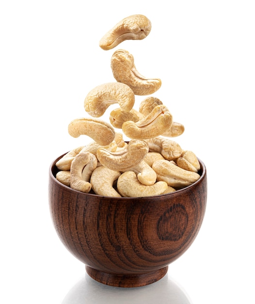 Falling cashew nuts into wooden bowl isolated on white background with clipping path