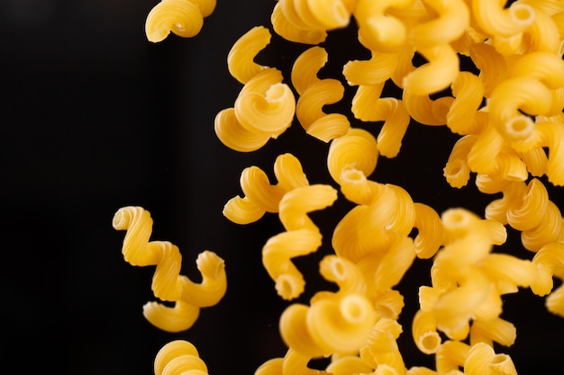 Falling cavatappi pasta. Flying yellow raw macaroni over black background. Shallow dof.