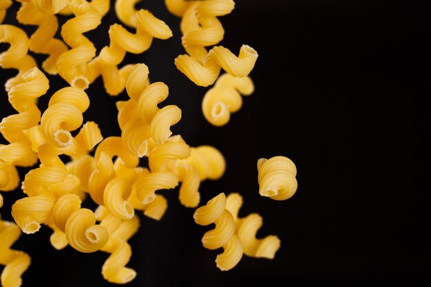 Falling cavatappi pasta. flying yellow raw macaroni over black background. shallow dof