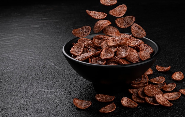 Falling chocolate corn flakes on black background, healthy cereal breakfast