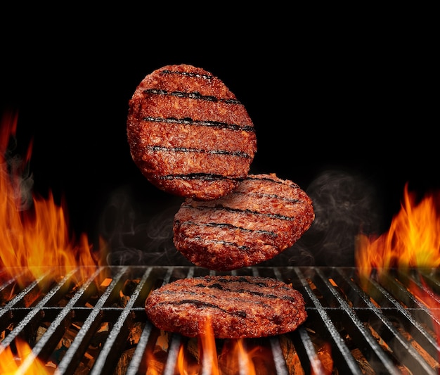 Falling down beef cutlets for burgers meat roasted on metal barbecue bbq grill with flaming fire and...