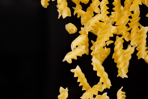 Falling fusilli pasta. Flying yellow raw macaroni over black background. Shallow dof.