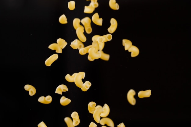 Falling gobetti pasta. Flying yellow raw macaroni over black background. Shallow dof.