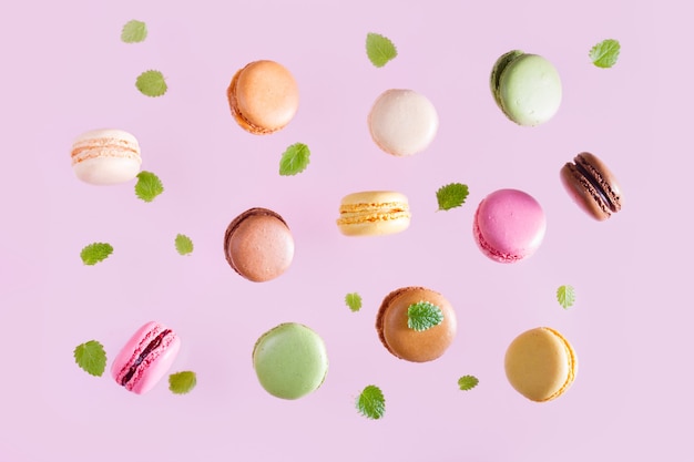 민트와 함께 떨어지는 macarons 분홍색 배경에 나뭇잎