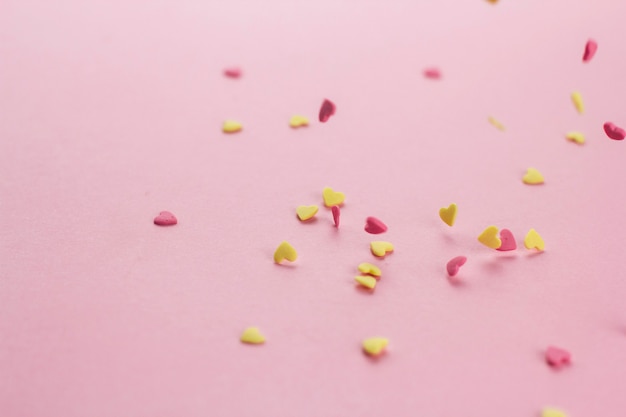 falling yellow and pink heart-shaped confectionery confetti on a pink background copy space