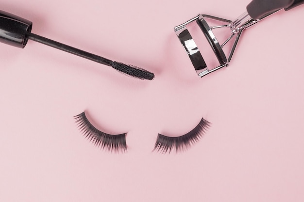 False eyelashes and curlers with a brush on a pink background