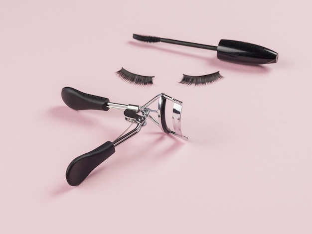 Photo false eyelashes between a makeup brush and curlers on a pink background