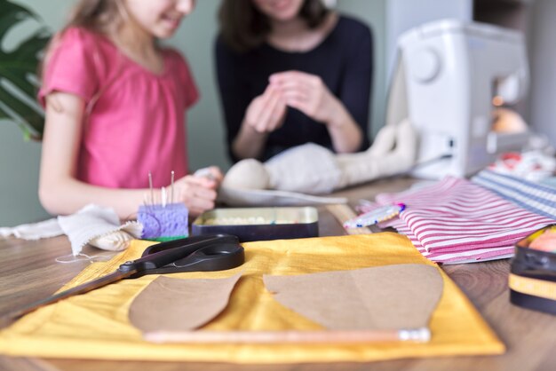 Foto familie creatieve handgemaakte hobby en vrije tijd, kinderen die thuis zitten, pop naaien, in defocus, achtergrond. close-up van stof, sjablonen, patronen, schaar, draden, naalden