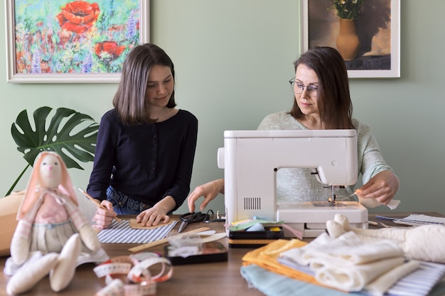 Familie creatieve handgemaakte hobby en vrije tijd, moeder en tienerdochter naaien samen konijnenspeelgoedpop. Vrouw leert meisje naaivaardigheden, praten