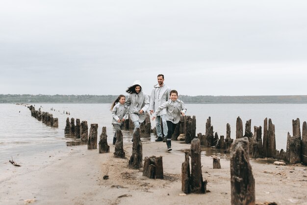 Familie die loopt en een pret dichtbij het overzees in regenjas heeft