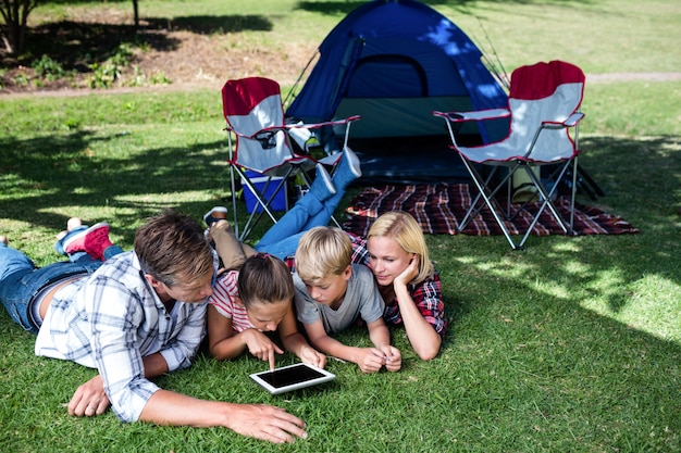 Foto familie die op gras ligt en digitale tablet gebruikt