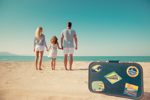 familie die op het strand staat en naar zee en lucht kijkt met een vintage koffer op de voorgrond