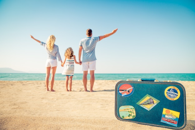 familie die op het strand staat en naar zee en lucht kijkt met een vintage koffer op de voorgrond