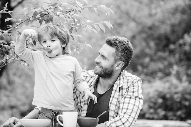 Familie diner tijd gelukkige vaders dag Kleine jongen met vader eet granen zomer picknick Ochtend ontbijt gezond eten en diëten Kinderdag vader en zoon eten buiten Gelukkig familie concept